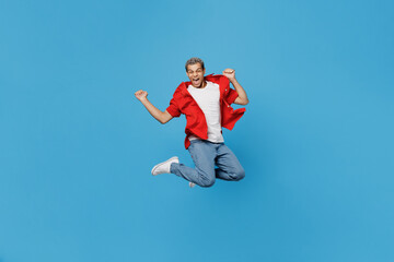Naklejka na ściany i meble Full body young overjoyed excited cool man of African American ethnicity 20s wear red shirt jump high do winner gesture isolated on plain pastel light blue cyan background. People lifestyle concept
