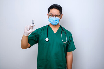 Excited asian male nurse in medical mask, rubber gloves and scrubs, looking amazed at syringe with vaccine