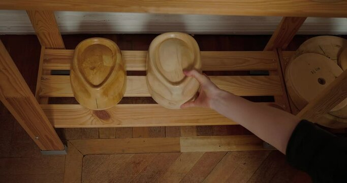 Milliner puts wooden molds for hats shape in row on shelf
