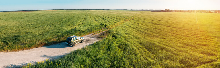 Obraz na płótnie Canvas Aerial view of car SUV parked near countryside road in field rural landscape. Aerial view of car SUV parked near countryside road on a sunny summer evening. Panorama, panoramic view.