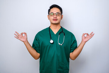 Calm and patient asian male doctor, nurse in scrubs staying relaxed, meditating with eyes closed and happy smile