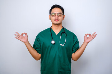 Calm and patient asian male doctor, nurse in scrubs staying relaxed, meditating with eyes closed...