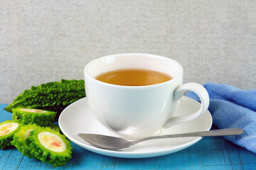 Bitter gourd or bitter melon tea in white cup on blue wooden and white background. Scientific name is Momordica charantia. As a whole food and herbs for treating diseases.