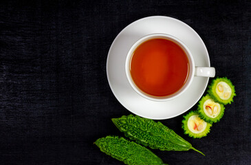 Bitter gourd or bitter melon tea in ceramic cup on black background, top view. Scientific name is Momordica charantia. As a whole food and herbs for treating diseases.