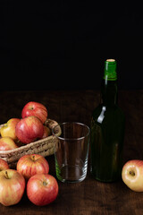 Bottle of cider next to an empty glass and some apples, the fruit from which the cider is extracted.