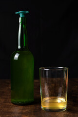 Bottle of cider with a pourer next to a glass with a little cider, with the normal amount that cider is usually served, also called culin.