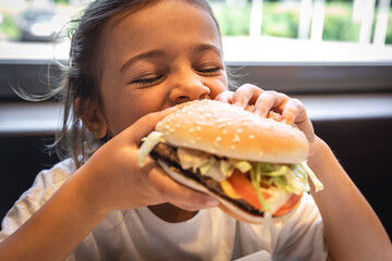 A little girl eats an appetizing burger, close-up.