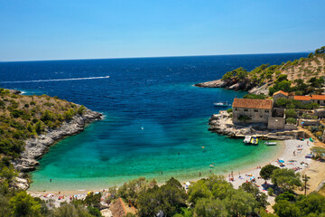 View on Dubovice Beach on the island of Hvar, Croatia with moored boats and many swimmers. Church and Beachbar below as well as a fishermans house.