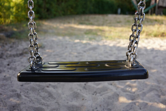 Close Up Of An Empty Swing In A Playground. Sandbox And Blurred Background. No People. Children's Playground Or Kindergarten