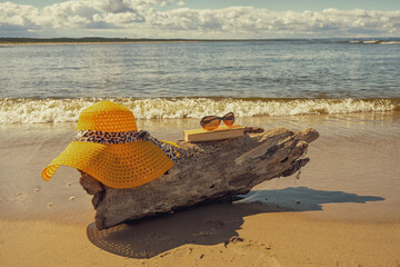 Akcesoria plażowe ułożone na kawałku drewna wyrzuconego na brzeg, wakacje, słoneczny plażowy dzień, morze, piasek. 