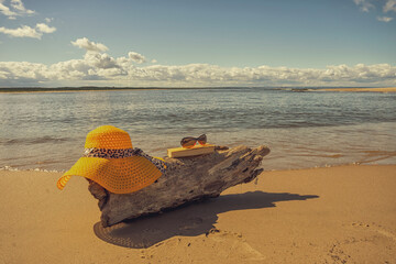 Akcesoria plażowe ułożone na kawałku drewna wyrzuconego na brzeg, wakacje, słoneczny plażowy dzień, morze, piasek.  - obrazy, fototapety, plakaty