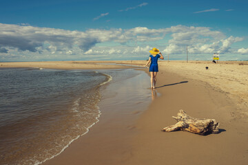 Dziewczyna w żółtym kapeluszu spacerująca po plaży. Pogodny słoneczny letni dzień, spokojna...