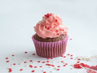 Delicious cupcake with a lush pink cream cap and culinary sprinkles on white