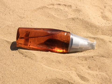 A Plastic Bottle Of Suntan Oil Lies On The Sand In The Bright Sun, A Place For Text, Hard Shadows