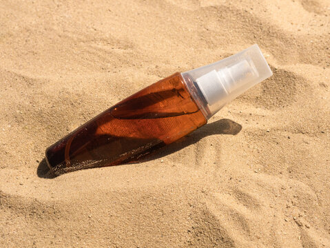 A Plastic Bottle Of Suntan Oil Lies On The Sand In The Bright Sun, A Place For Text, Hard Shadows