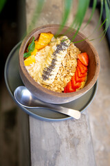 Mango smoothies bowl with berries, granola, chia seeds and coconut on concrete background with palm in front.