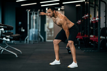 Fototapeta na wymiar Handsome Muscular Black Sportsman Exercising With Kettlebell At Modern Gym Interior