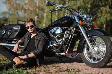 Fototapeta na wymiar Young male biker sitting on the ground with his motor bike