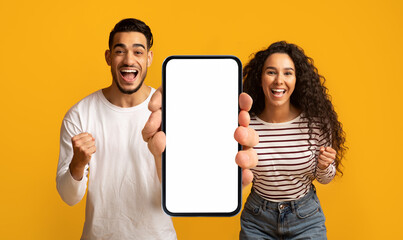 Happy emotional millennial arab couple enjoy online victory, show big smartphone with empty screen