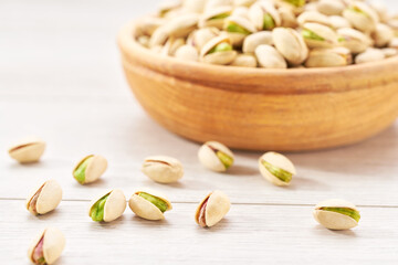 pistachios spill out of a wooden bowl on a white table.