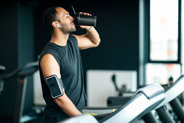 Black Man Drinking From Shaker Bottle While Jogging At Treadmill At Gym