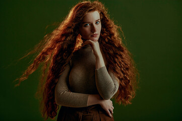 Beautiful freckled redhead woman with natural long curly hair wearing beige turtleneck, posing...