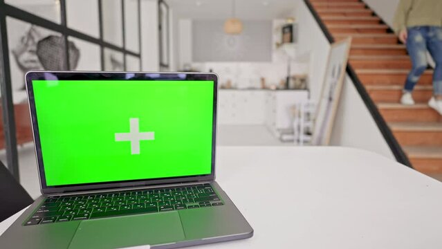 laptop with green screen in the kitchen on the background defocused woman going down stairs