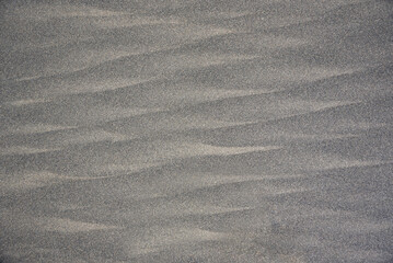 Grey textured background of river and sea sand as in the desert with natural patterns from the wind