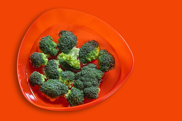 Top view on fresh green broccoli on orange color bowl. Healthy food.