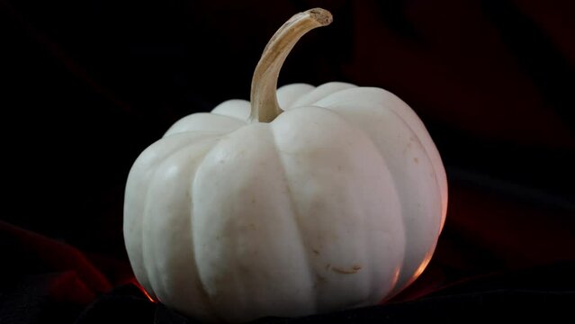 A white pumpkin decorated for Halloween rotates on a black background. The red light is on from below.