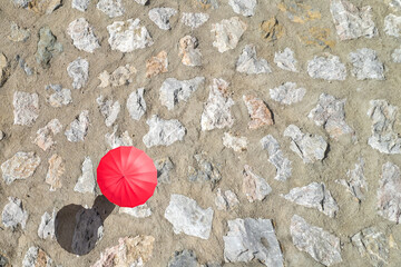Woman with red rain umbrella walking on the paved stone road protecting herself from the sun at...