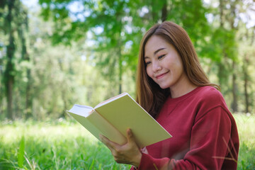 Portrait of a beautiful young asian woman reading a book while sitting in the park