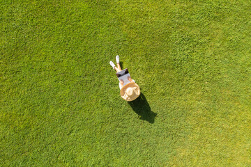 Woman in a white dress, hat with laptop, sitting on the green grass at summer day. Top view, drone,...