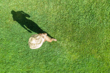 Obraz premium Woman in a white bikini and hat, walking on the green grass sunbathes at summer day. Top view, drone, aerial view