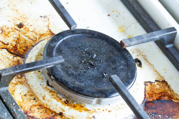 Dirty gas stove surface. Gas burner and cast iron grate of a gas oven surrounded by old leftovers of food and drinks. Top area surface and burner heads needs cleaning from burnt-on grease. Close-up