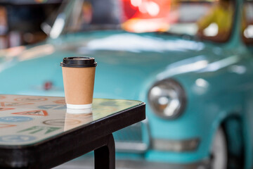 Eco-friendly paper coffee cup with a black lid on a retro car background. Street fast food. A fast food restaurant in the fresh air. Zero waste, plastic-free concept.