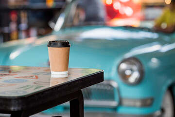 Eco-friendly paper coffee cup with a black lid on a retro car background. Street fast food. A fast food restaurant in the fresh air. Zero waste, plastic-free concept.