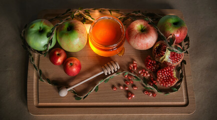 Traditional Jewish new year food. Happy Rosh Hashanah concept. Red and green apples, pomegranate and seeds and honey in a glass jar on wooden background.