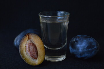 A glass of homemade plum brandy surrounded by ripe organic plums on a black background. Traditional...