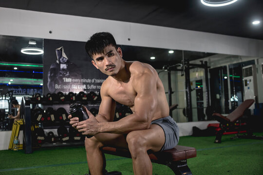 A robust muscled man with a tight waist sitting on the bench, contemplating on his next workout at the gym.