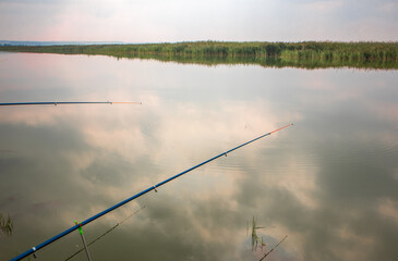 Two fishing rods reflected in the water surface, the reflection of clouds. A quiet hobby
