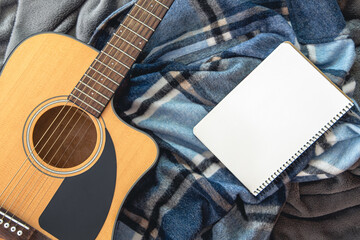 Acoustic guitar and notepad on a plaid background, top view.