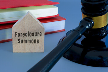 Judge gavel with foreclosure summons word on wooden house on blue background.