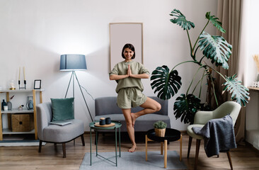Sportswoman taking Tree pose in living room