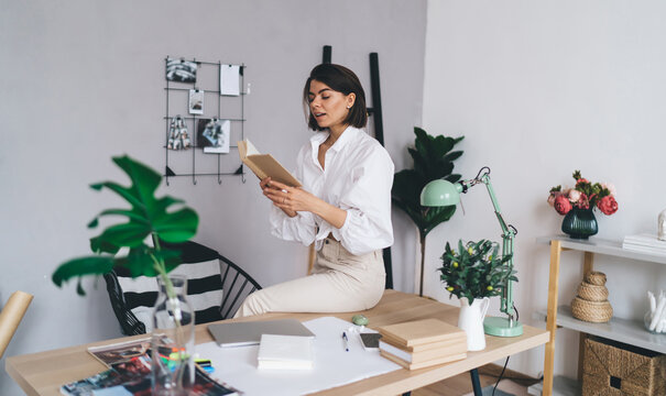 Young lady reading book aloud while working in modern workspace
