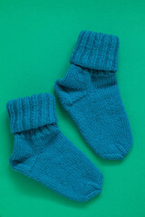 Two knitted wool turquoise socks for winter on a green background. Top view.