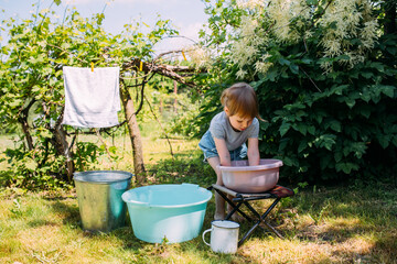 Naklejka na ściany i meble Little preschool girl helps with laundry. Child washes clothes in garden