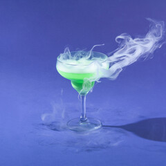 Minimal 2022 Halloween party concept with neon green ice cold martini drink on dark purple background. Celebration and smoking cocktail aesthetic. Magic potion idea.