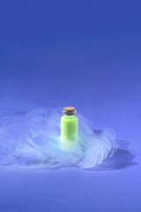 Minimal 2022 Halloween magic potion drink concept with foggy neon green liquid in glass bottle on purple blue background. Science and smoking cocktail aesthetic.
