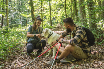 Young happy couple and their dog at hiking through the woods enjoying the sight. Two nature lovers in the mountain forest enjoy healthy walking through the nature. With film grain selective focus